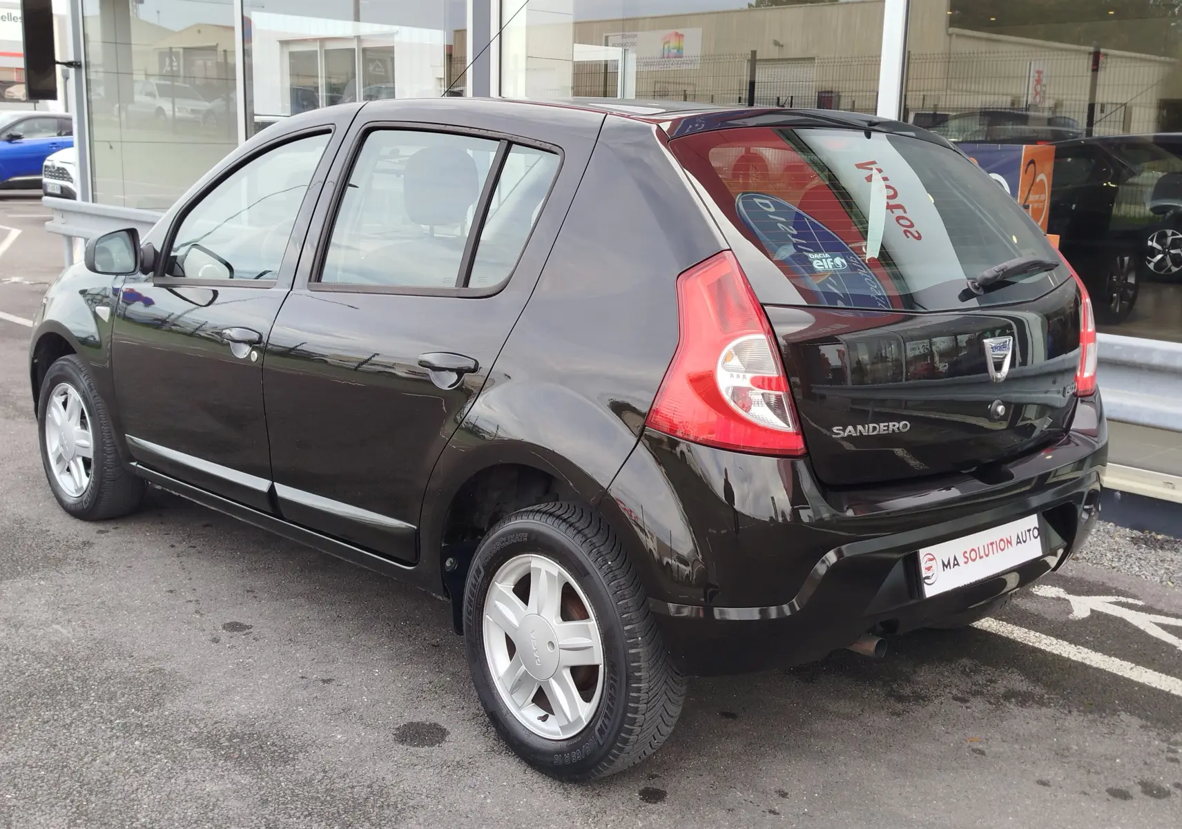 Vue 3/4 arrière droite d'une Dacia Sandero noire 5 portes de 2011 avec jantes alliage et feux arrière distinctifs.