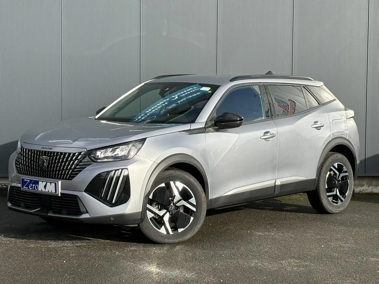 Peugeot 2008 Hybrid 145 e-DSC6 Allure gris Artense, vue 3/4 avant avec jantes alliage bi-ton et barres de toit noires.
