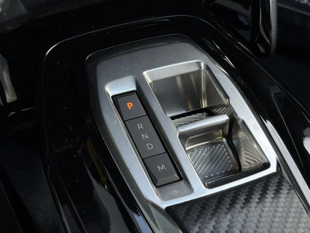 Gros plan sur la console centrale noire brillante du Peugeot 2008 Hybrid 145 avec sélecteur de boîte automatique.