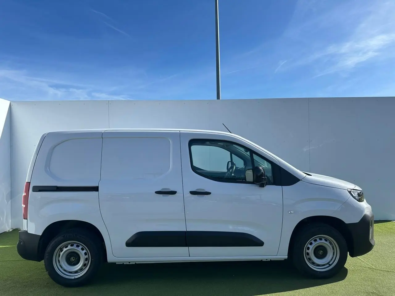 Vue 3/4 avant d'un utilitaire Citroën Berlingo blanc Icy avec pare-chocs noir devant un bâtiment Distinxion.