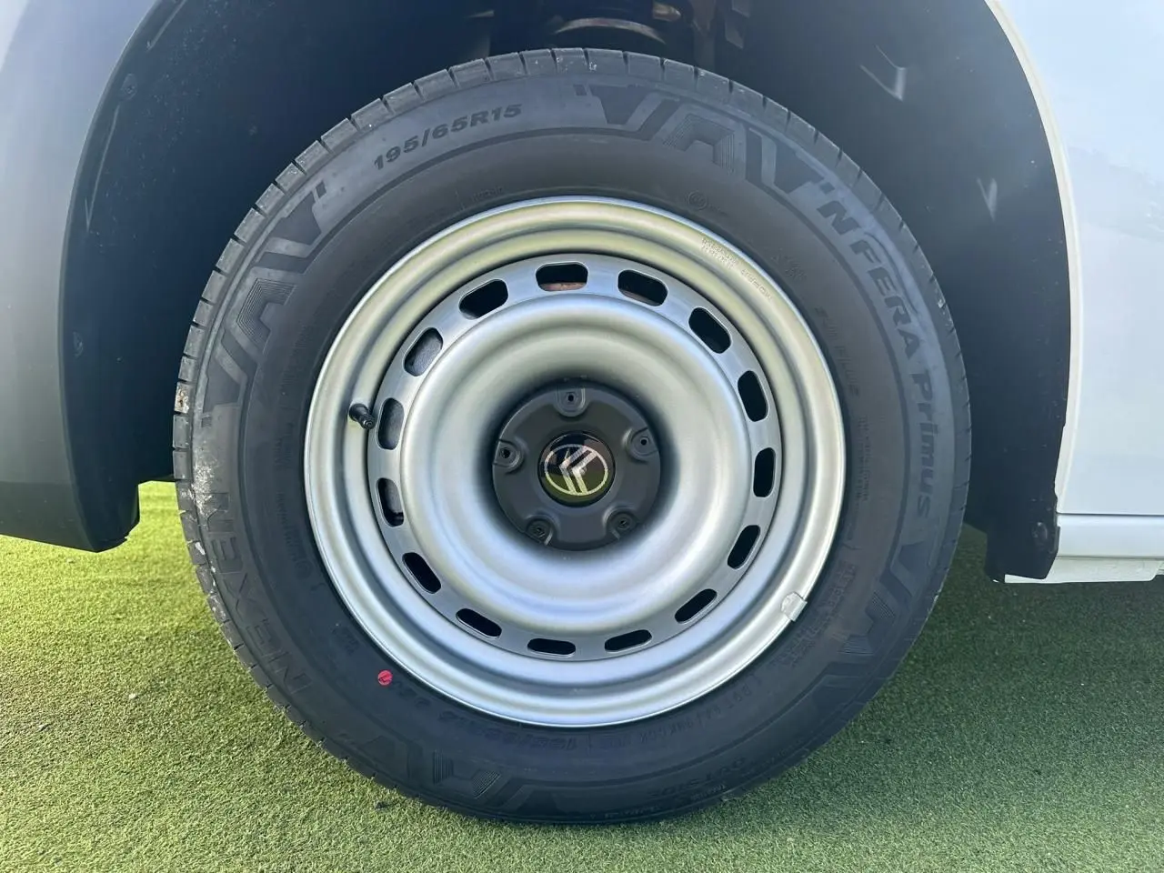 Gros plan sur la roue arrière droite en jante tôle grise du Citroën Berlingo blanc Icy, avec logo Citroën central.