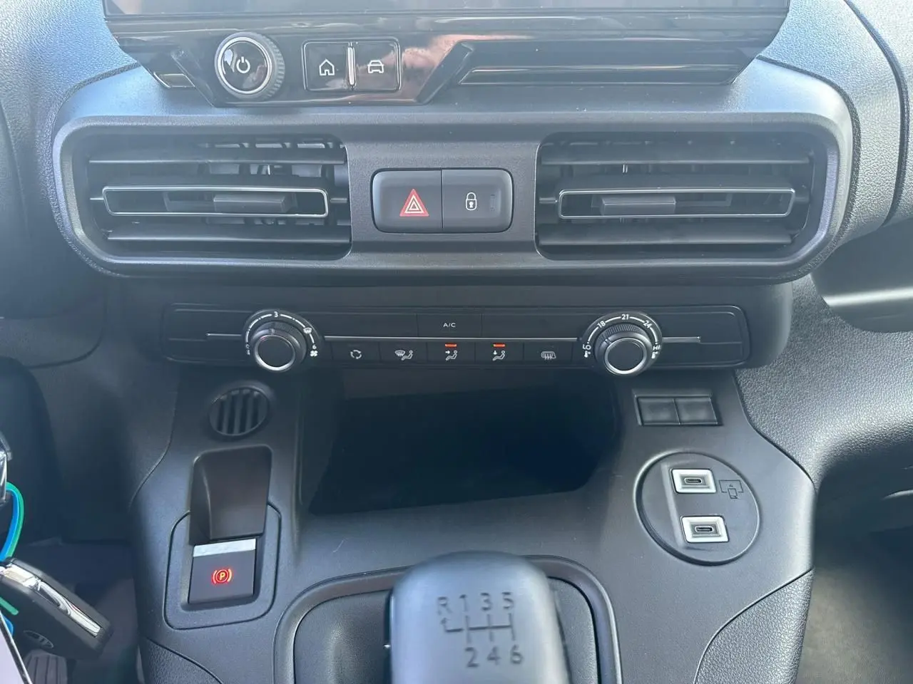 Vue rapprochée du tableau de bord et console centrale noire du Citroën Berlingo blanc, avec boîte manuelle et commandes climatisation.