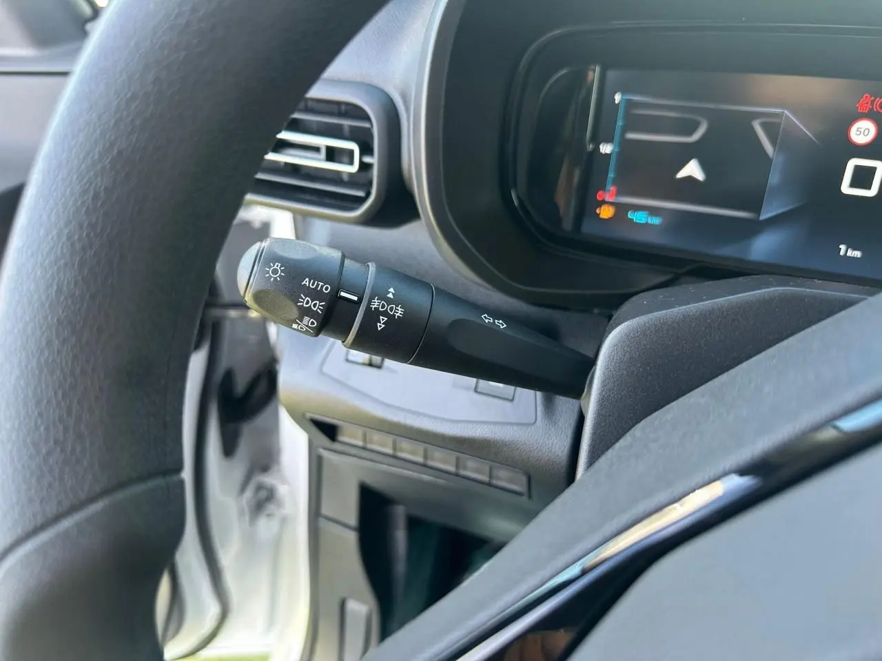 Vue rapprochée du combiné numérique 10'' et du commodo d'éclairage du Citroën Berlingo blanc, côté conducteur.