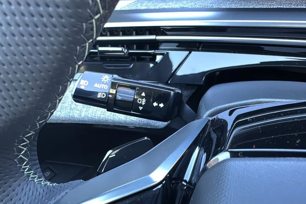 Gros plan sur la commande des feux et clignotants côté gauche du volant cuir perforé du Peugeot 3008 blanc okénite.