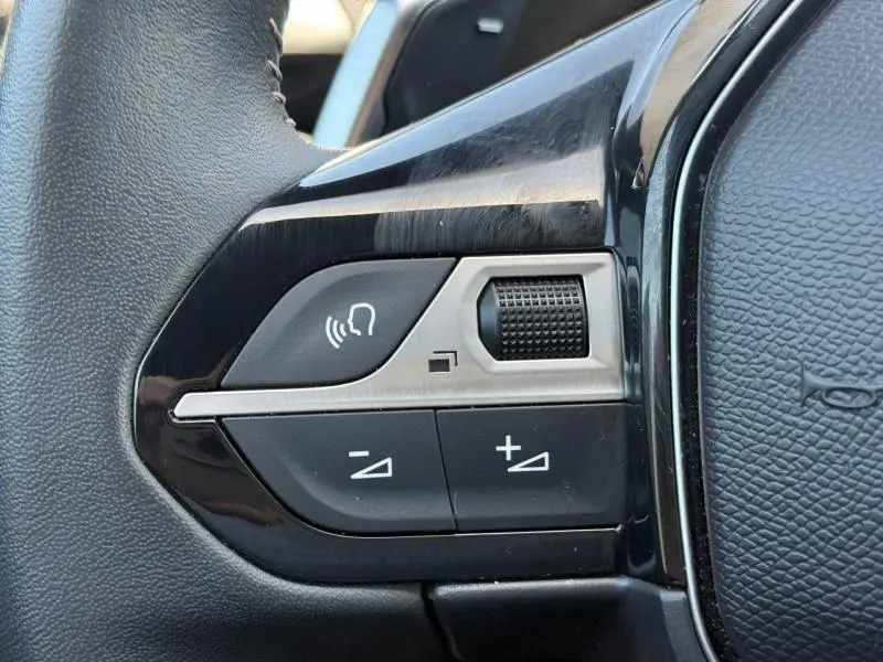 Gros plan sur les commandes du volant cuir noir du Peugeot 3008 Hybride Rechargeable 2024, boutons de volume et fonction mains-libres.