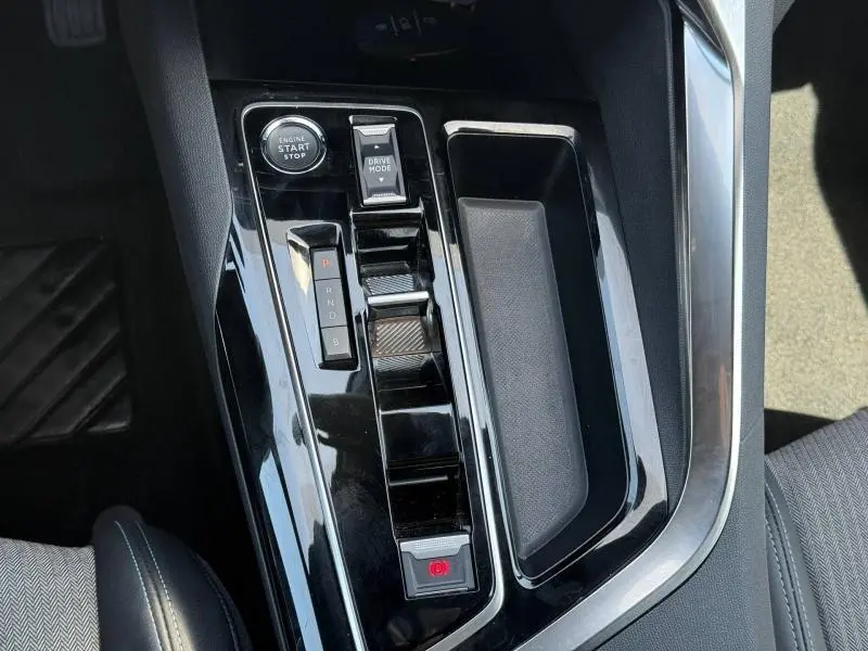 Vue rapprochée de la console centrale noire brillante du Peugeot 3008 Hybride Rechargeable avec boutons start/stop et sélecteur de mode de conduite.