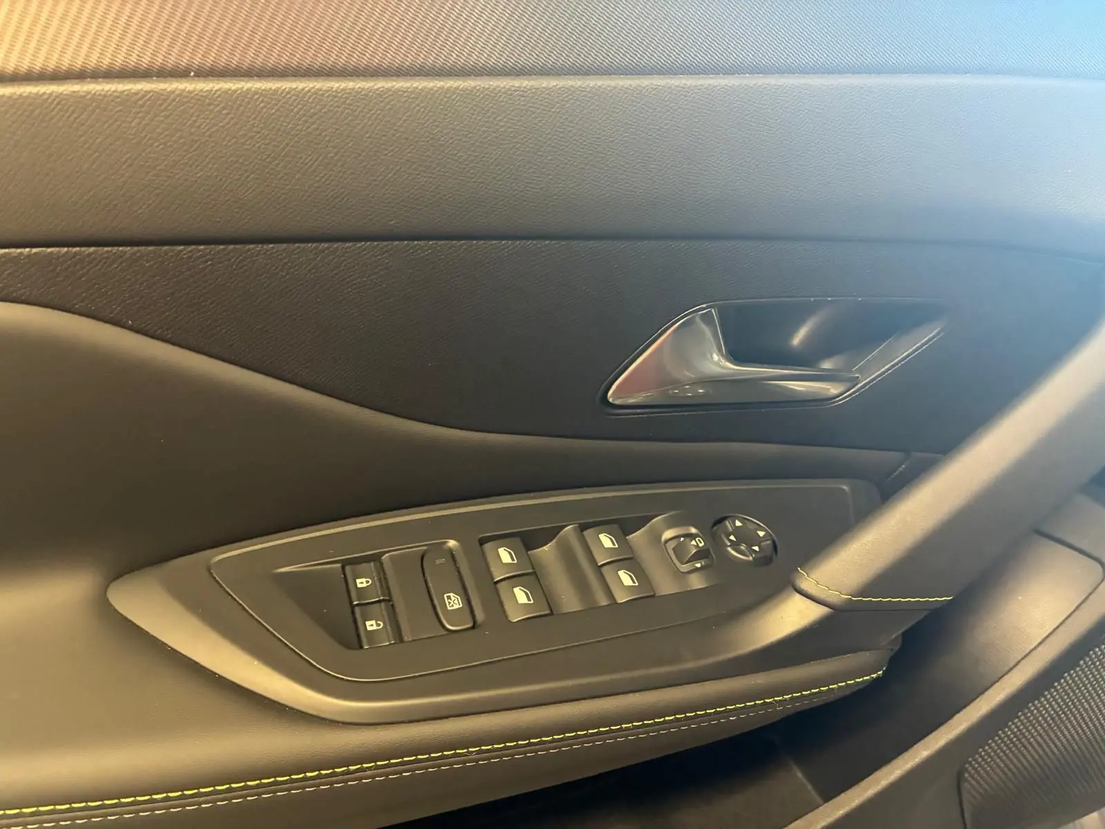 Gros plan sur la porte côté gauche intérieure de la Peugeot 308 gris, avec commandes électriques et surpiqûres vertes.