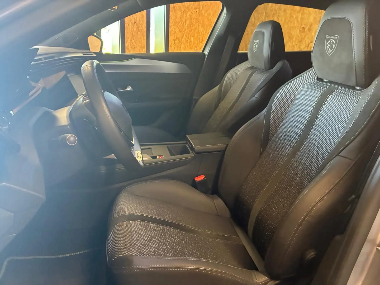 Vue intérieure côté conducteur de la Peugeot 308 gris 2025, sièges noirs avec logo Peugeot brodé sur les appuie-têtes.