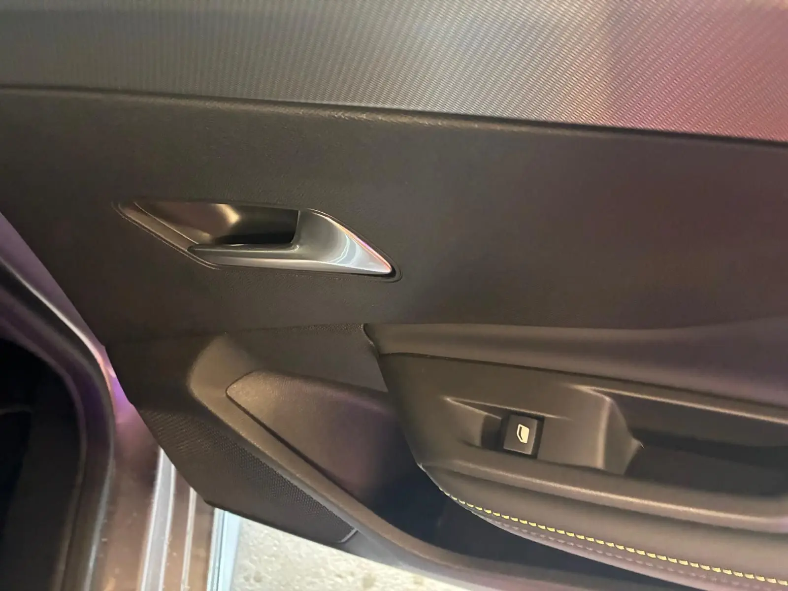 Détail de la porte intérieure côté gauche de la Peugeot 308 gris, avec poignée argentée et bouton de commande de vitre.