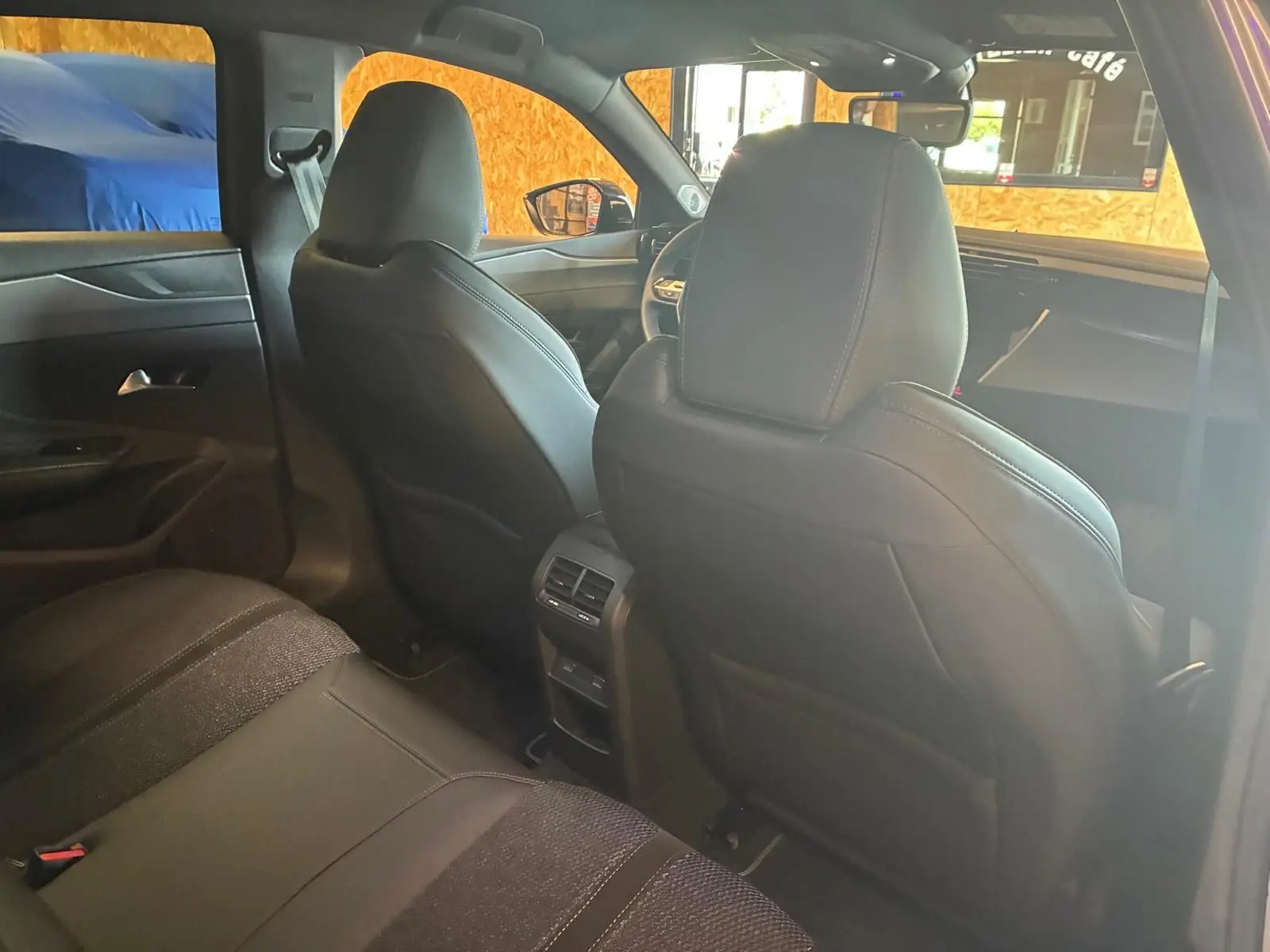 Vue intérieure arrière de la Peugeot 308 hybride 2025, sièges noirs et console centrale avec aérateurs visibles.