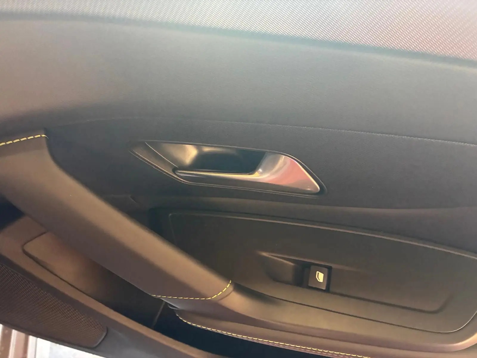 Détail de la porte intérieure côté gauche de la Peugeot 308 gris, avec poignée argentée et couture jaune visible.