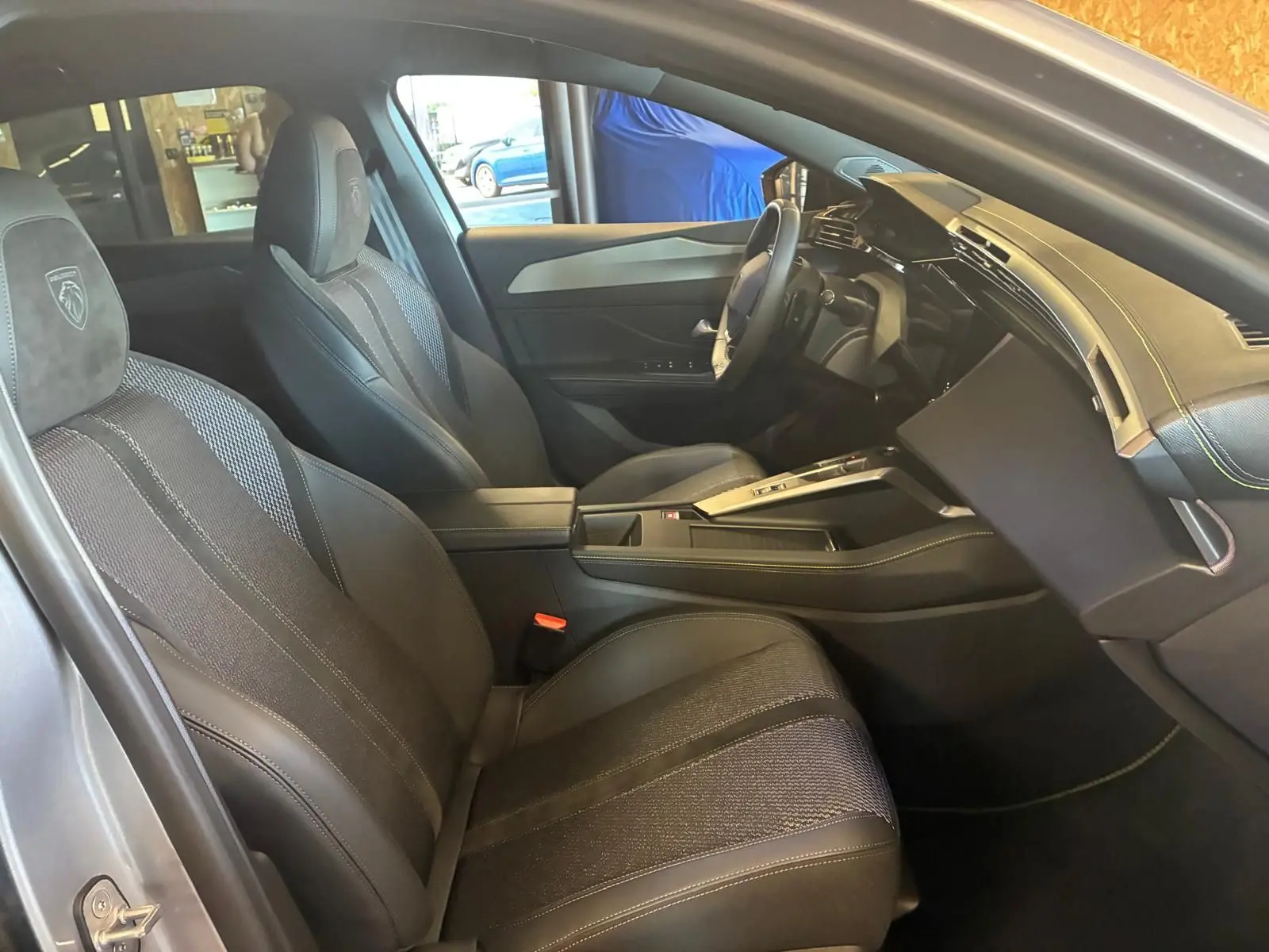 Vue intérieure côté conducteur de la Peugeot 308 gris 2025, sièges noirs avec surpiqûres et tableau de bord moderne.