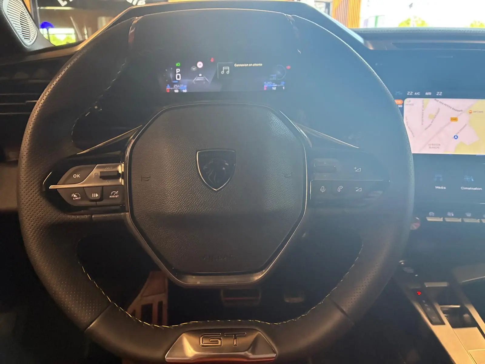 Vue rapprochée du volant cuir noir avec logo Peugeot et badge GT, tableau de bord numérique et écran tactile de navigation visibles.