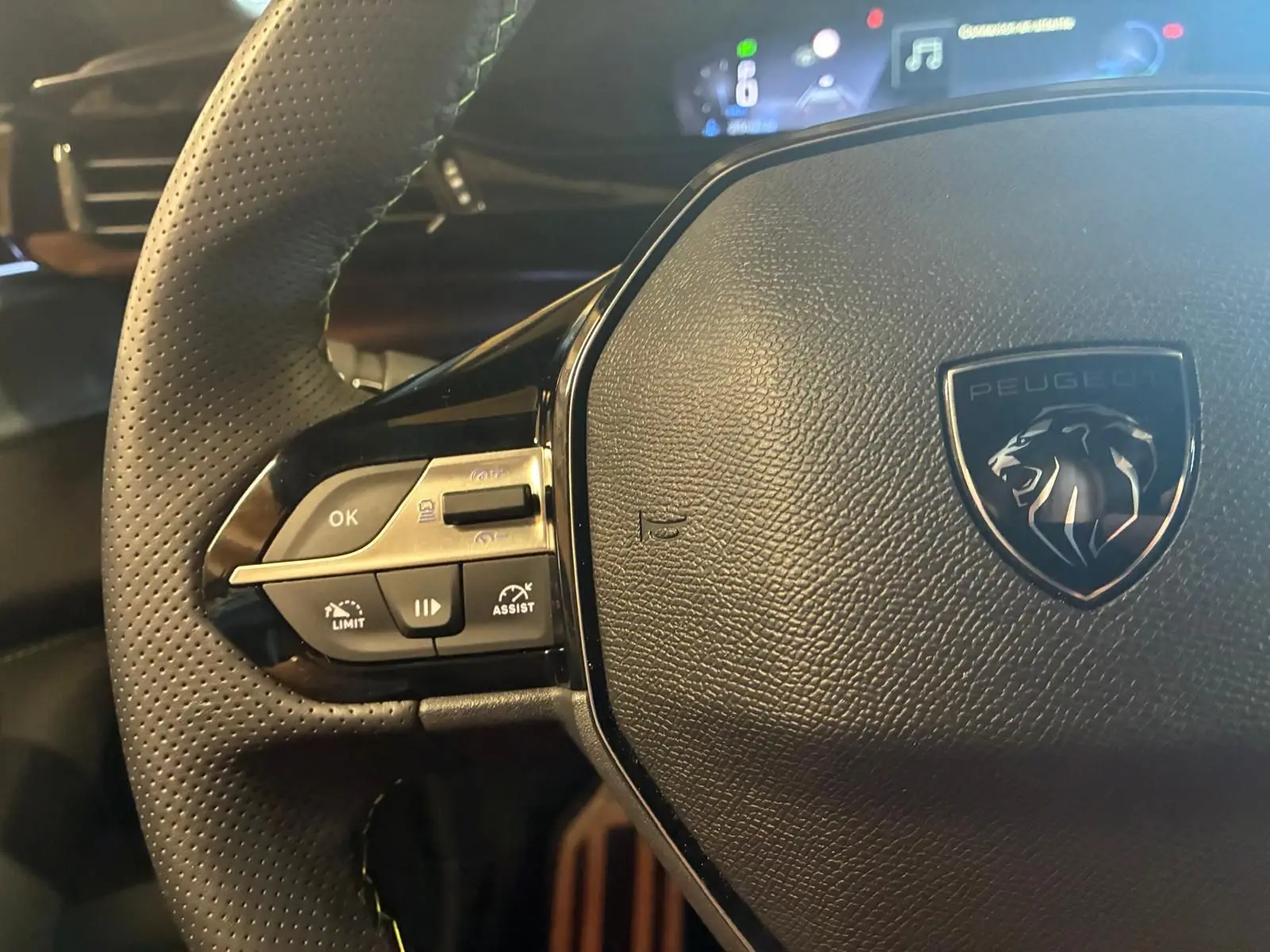 Gros plan sur le volant noir perforé de la Peugeot 308 1.2 HYBRID 136 GT avec commandes intégrées et logo lion central.
