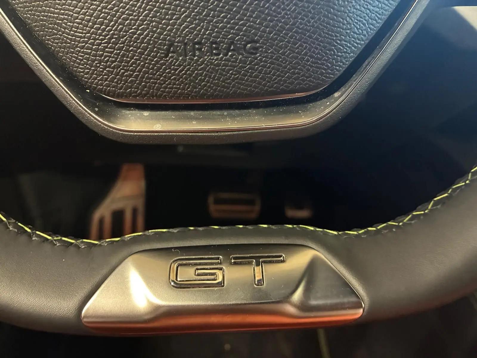 Gros plan sur le volant noir avec surpiqûres vertes et logo GT de la Peugeot 308 1.2 Hybrid 136 E-DCS6 GT.
