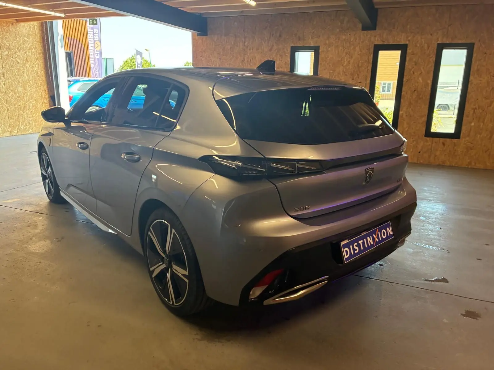 Vue 3/4 arrière droite d'une Peugeot 308 gris métallisé 2025 en hybride, avec feux arrière noirs et jantes sport.