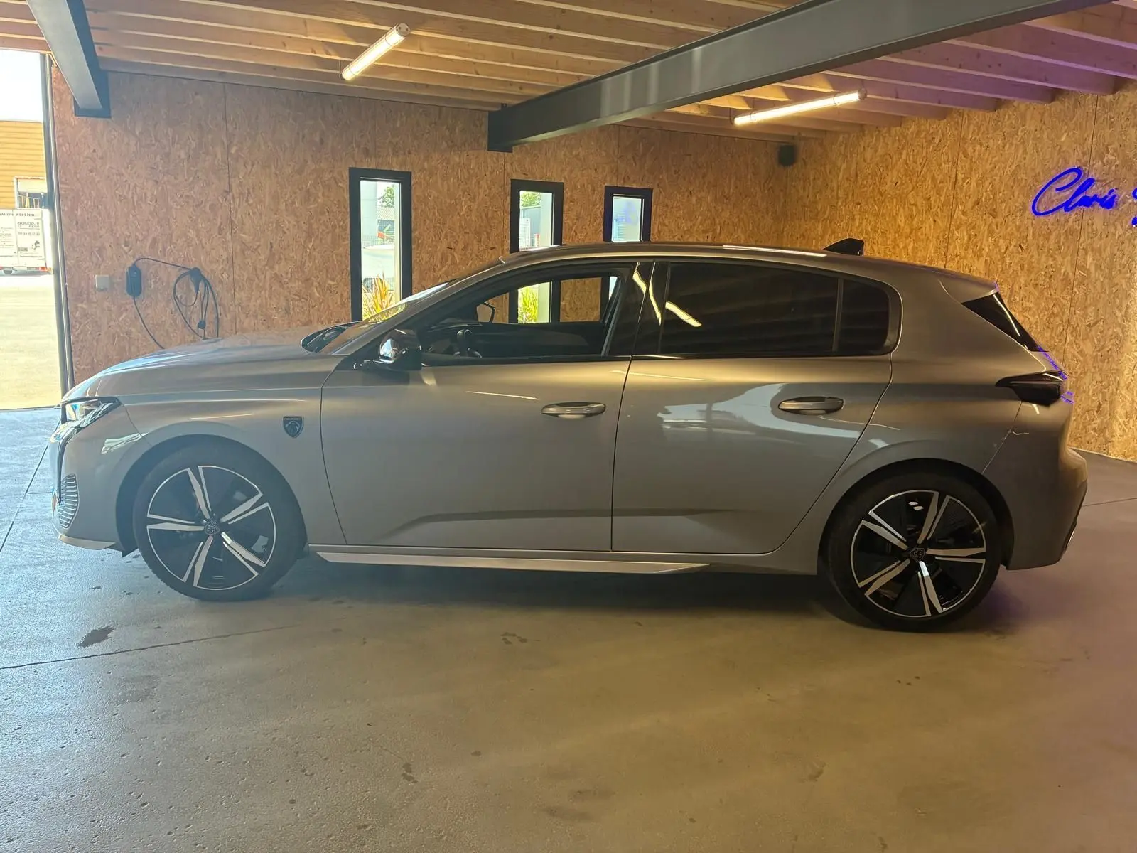 Peugeot 308 1.2 Hybrid gris vue de profil côté gauche, avec jantes noires et toit noir en intérieur d'atelier.