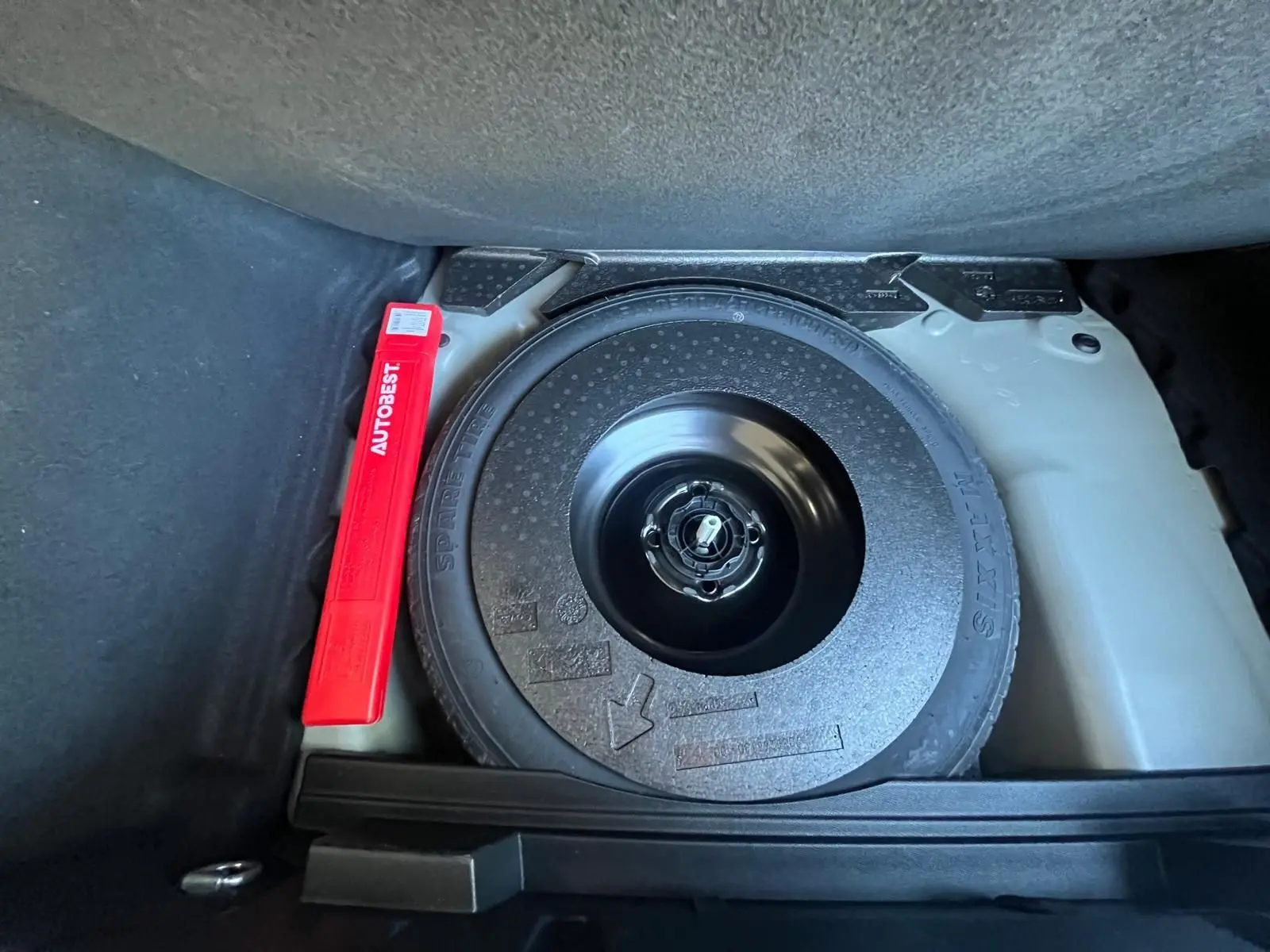 Gros plan sur la roue de secours et le triangle de signalisation rouge dans le coffre du DS3 Crossback Performance Line gris.