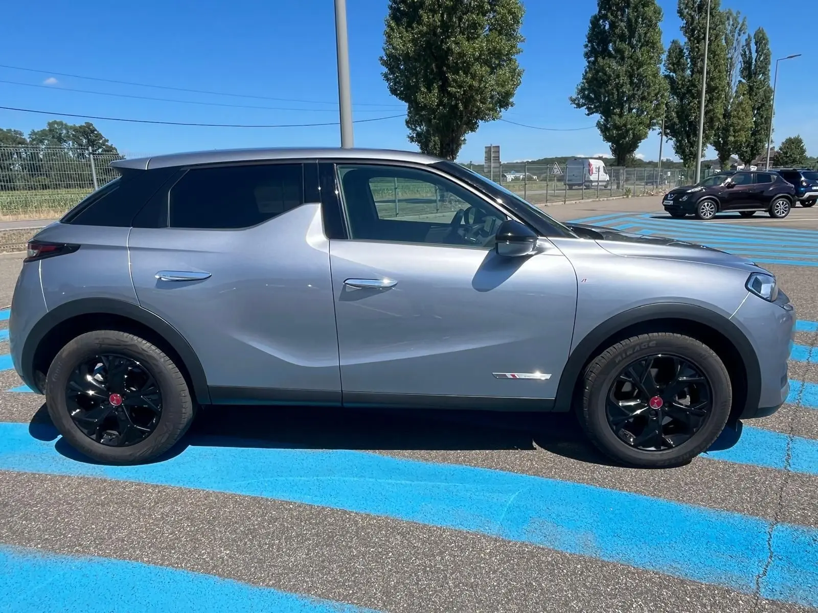 Vue latérale côté gauche d'un DS3 Crossback Performance Line gris métallisé avec jantes noires sur un parking.