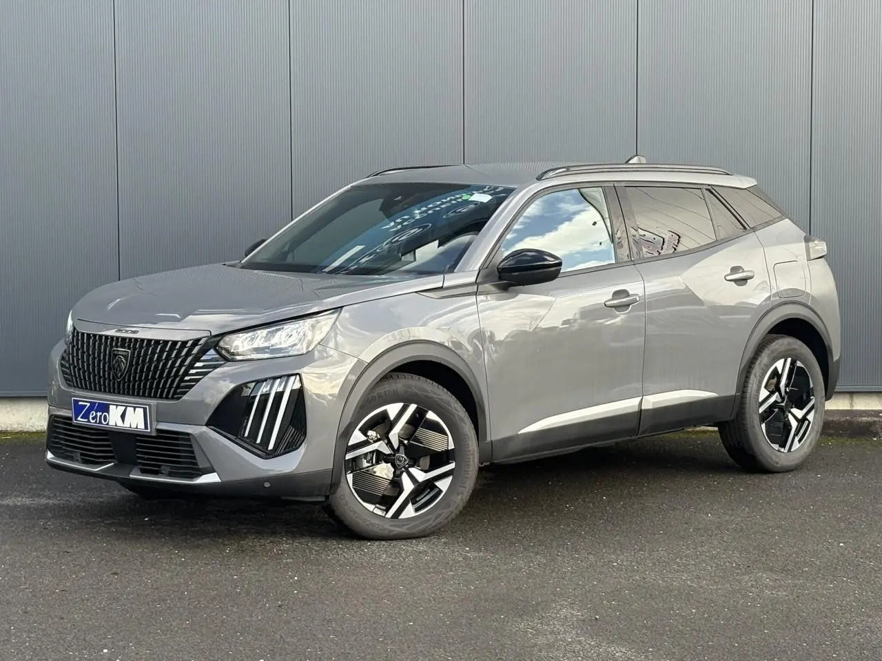 Peugeot 2008 Hybrid 145 e-DSC6 Allure gris Selenium en 3/4 avant droit avec jantes alliage bi-ton et barres de toit noires.