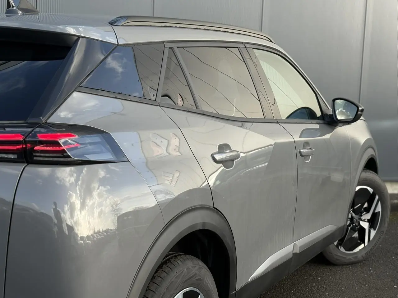 Peugeot 2008 Hybrid 145 e-DSC6 Allure gris Selenium, vue 3/4 arrière droit avec jantes alliage bi-ton et barres de toit noires.