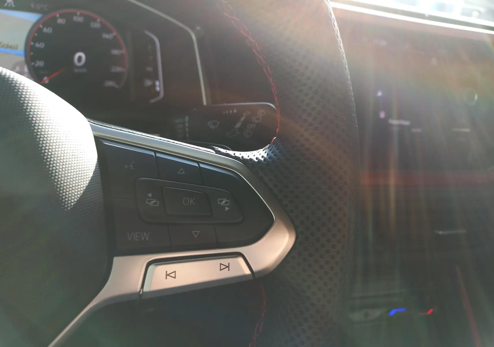 Gros plan sur le volant perforé avec surpiqûres rouges du Volkswagen Polo GTI 2024, tableau de bord et commandes visibles.