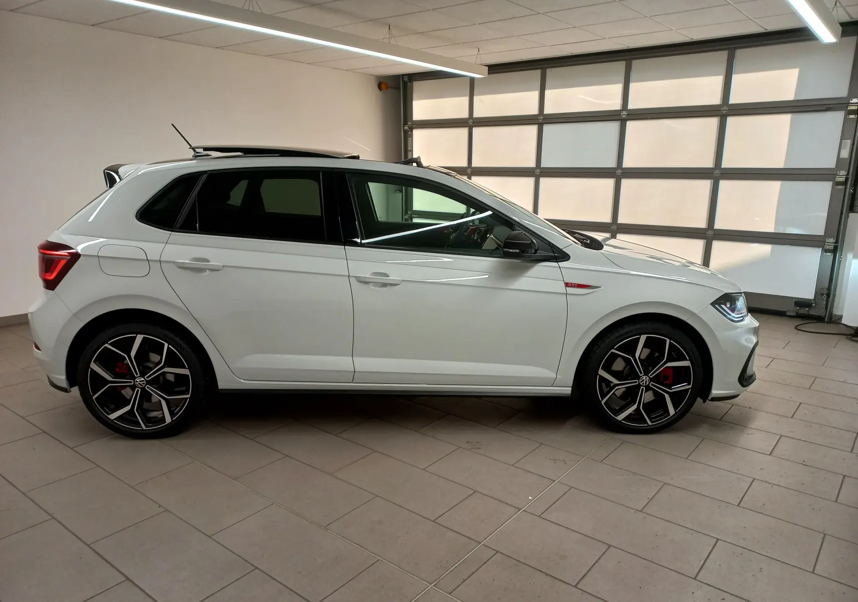 Vue de profil côté gauche d'une Volkswagen Polo GTI 2024 blanche avec toit noir et jantes sport en intérieur.