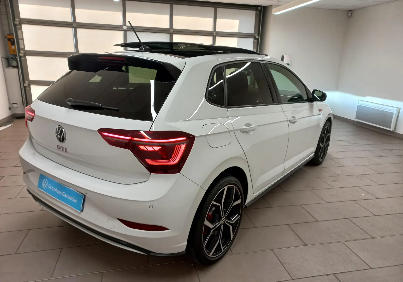 Volkswagen Polo GTI blanc pur avec toit noir, vue 3/4 arrière droit, feux allumés et jantes sport noires.