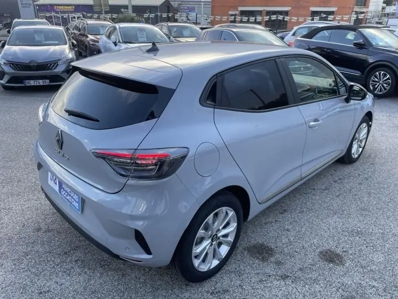 Vue 3/4 arrière droite d'une Renault Clio V gris métal 2025 avec vitres teintées et feux arrière LED allumés.