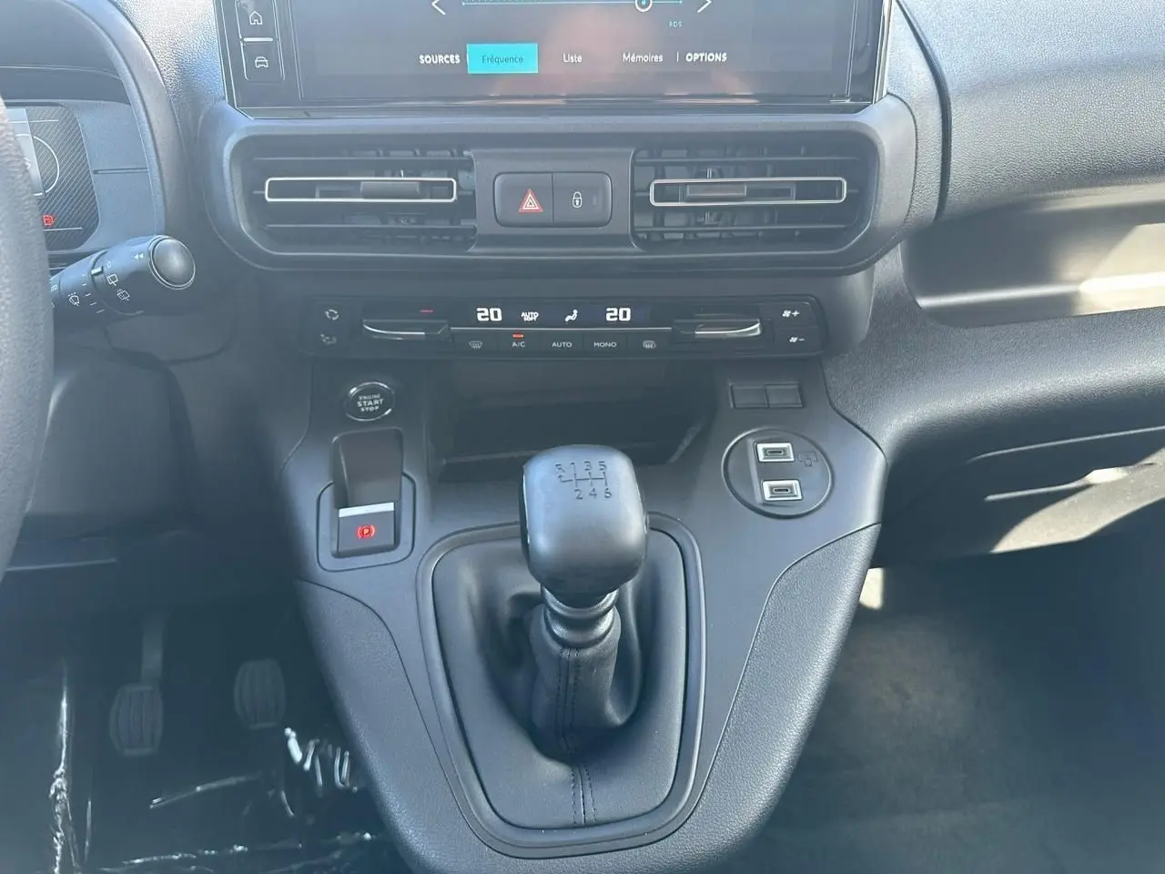 Gros plan sur la console centrale noire du Citroën Berlingo blanc, mettant en valeur le levier de vitesse manuel et l'écran tactile.