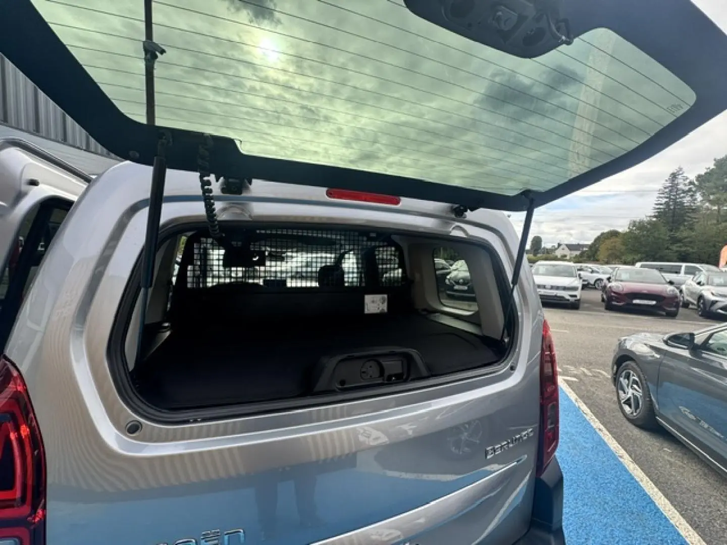 Vue arrière ouverte du Citroën Berlingo gris acier, montrant l'espace de chargement avec séparation intérieure.