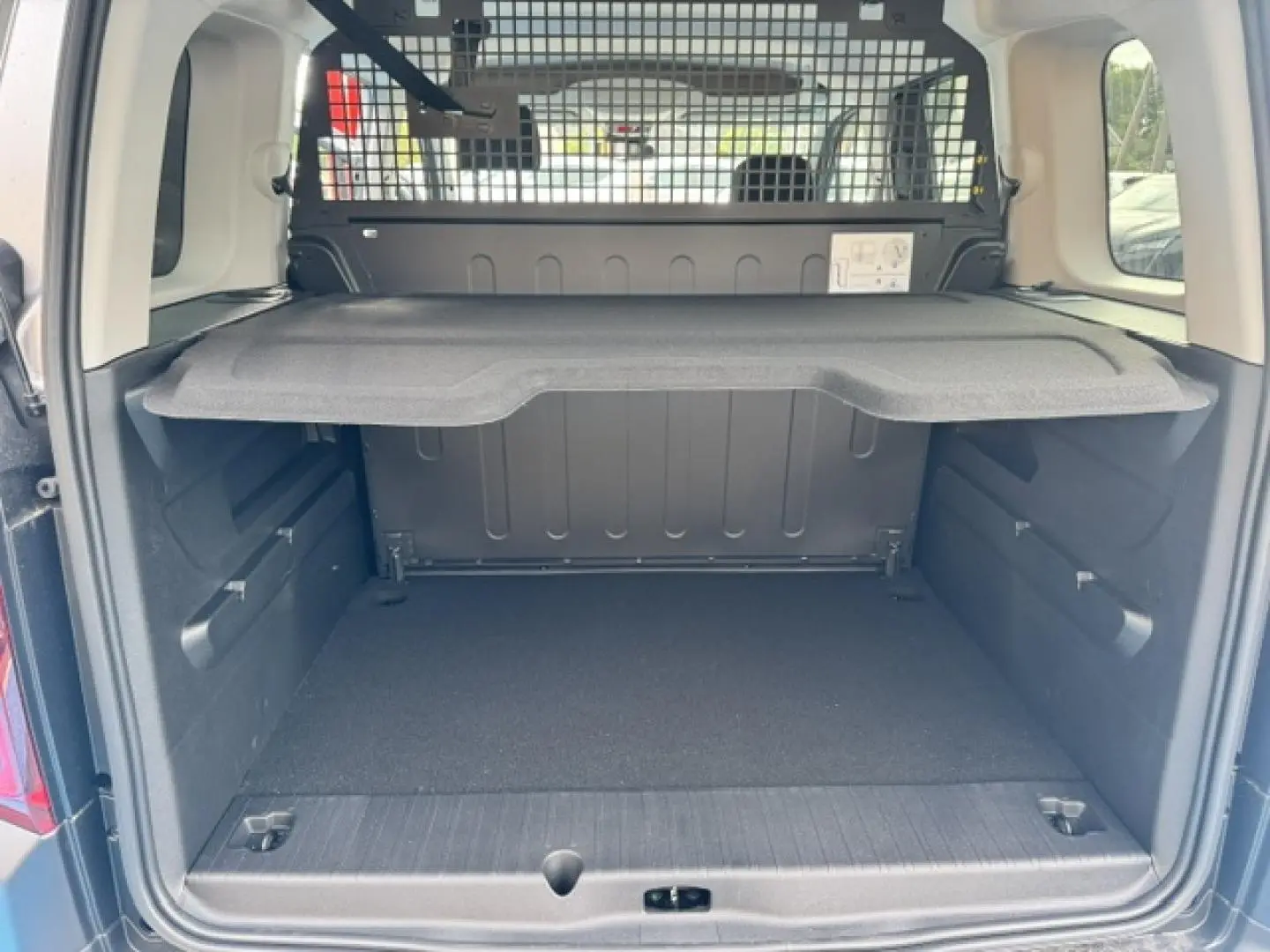 Coffre ouvert vu de l'arrière d'un Citroën Berlingo gris acier avec tablette de séparation et grille de protection.