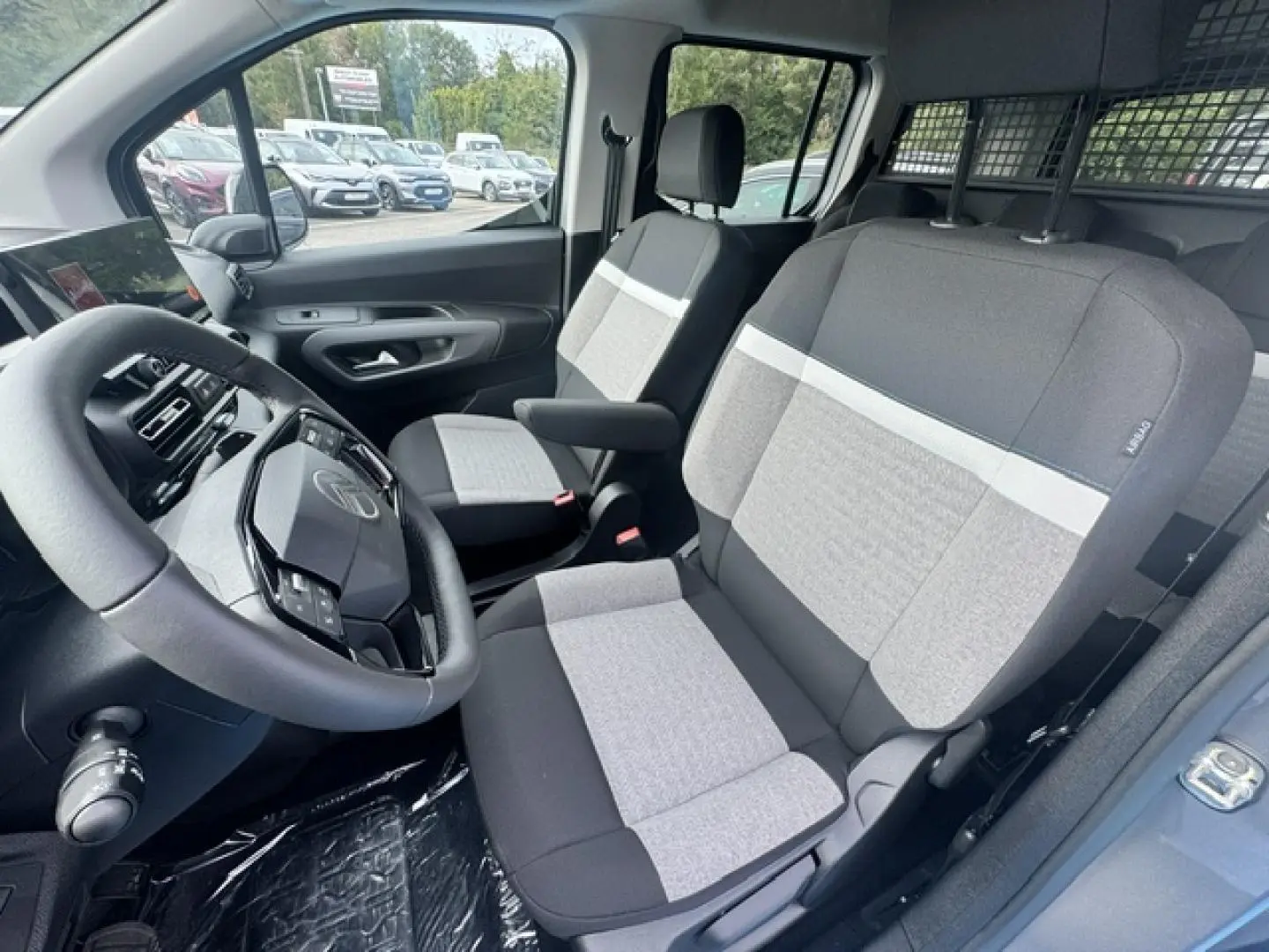 Intérieur avant du Citroën Berlingo gris acier, vue côté conducteur montrant les sièges tissu bicolore et le volant multifonction.
