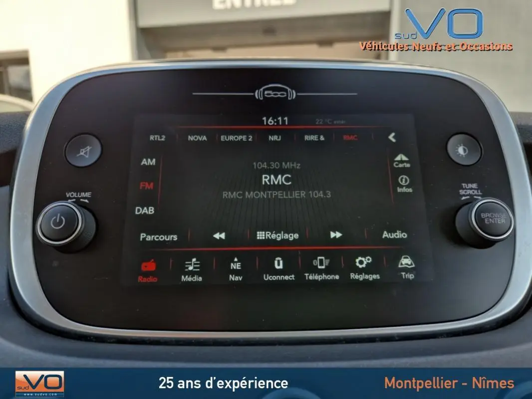 Vue de face de la console multimédia tactile du Fiat 500X gris clair, affichant la radio RMC à 104.3 MHz