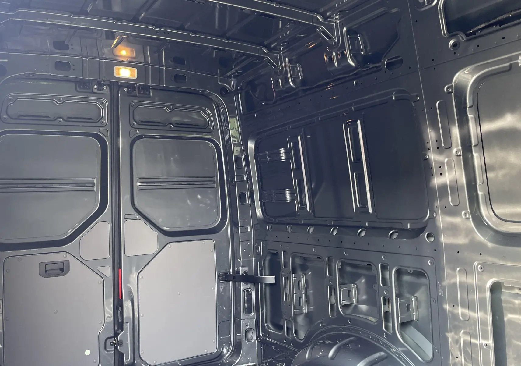 Vue intérieure arrière du Volkswagen Crafter van gris Indium montrant la cloison avec vitre fixe et l'espace de chargement métallique.