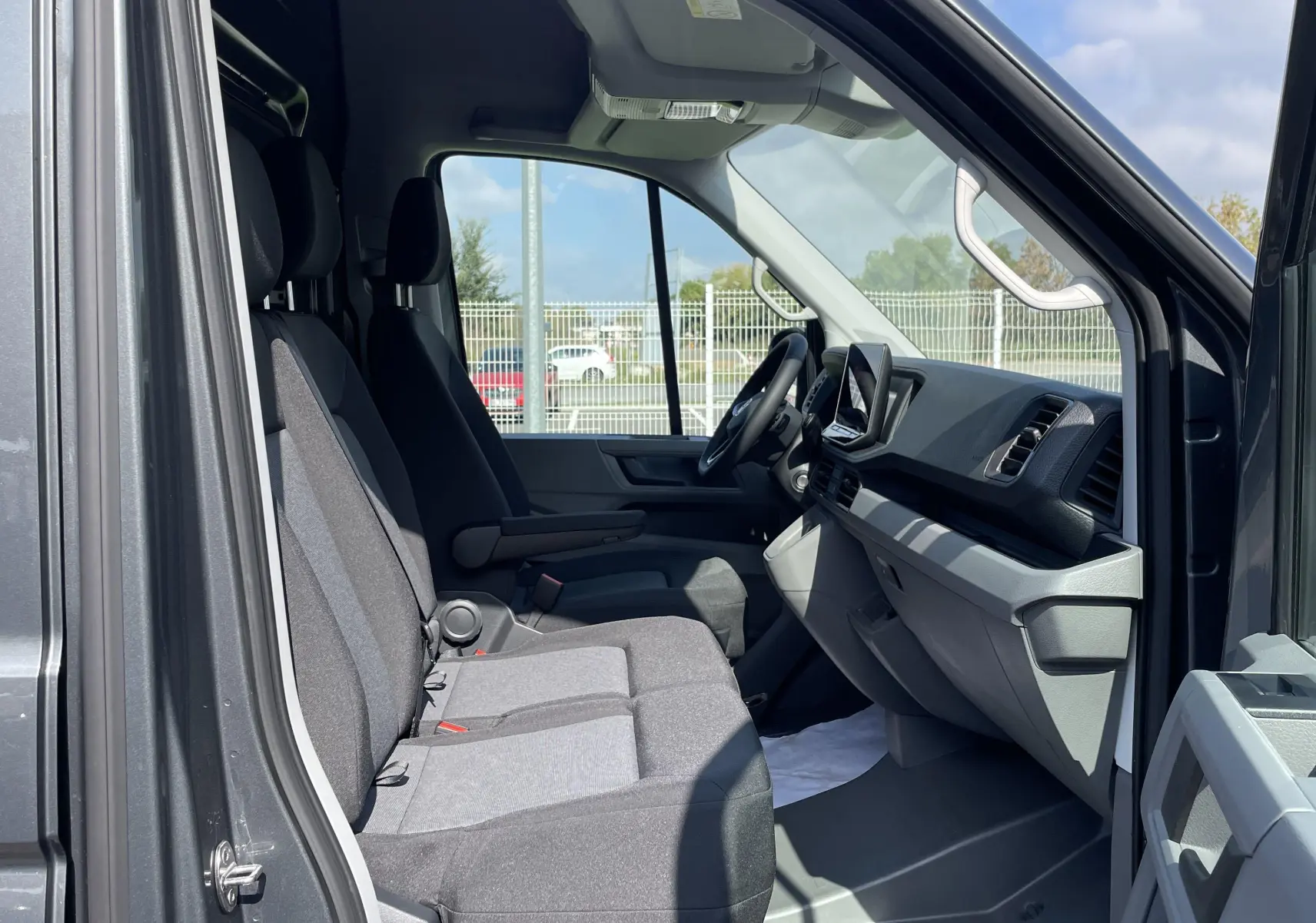 Vue latérale intérieure du Volkswagen Crafter gris Indium montrant les sièges avant et le tableau de bord moderne.