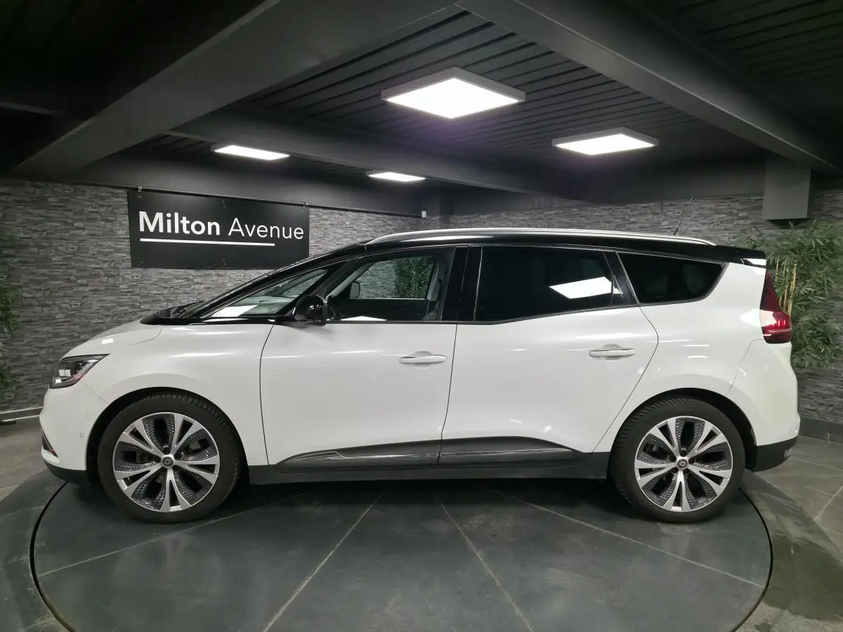 Profil droit d'un Renault Scénic blanc nacré avec toit noir et jantes alliage 20 pouces dans un showroom.