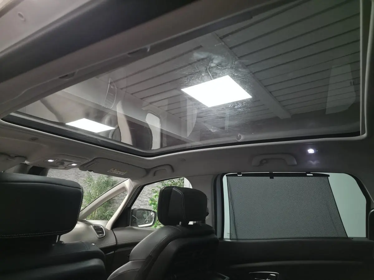Toit panoramique en verre du Renault Scenic Grand blanc, vue intérieure arrière avec sièges cuir carbone foncé et pare-soleil.