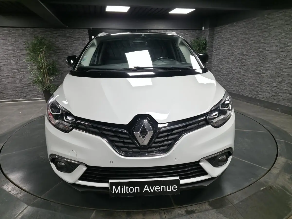 Vue frontale d'un Renault Scénic blanc nacré avec calandre noire et phares Full LED dans un showroom.