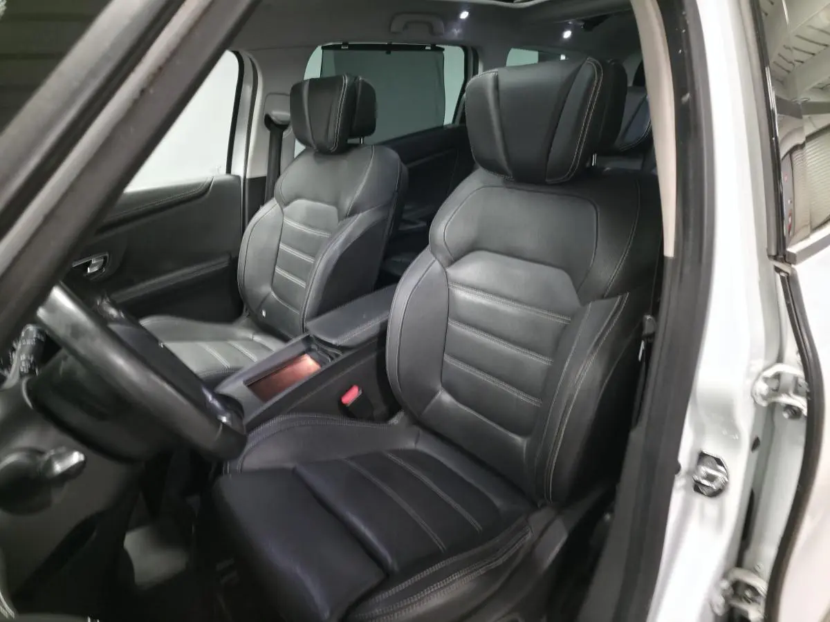 Intérieur vue côté conducteur d'un Renault Scenic blanc avec sièges cuir carbone foncé et accoudoir central.