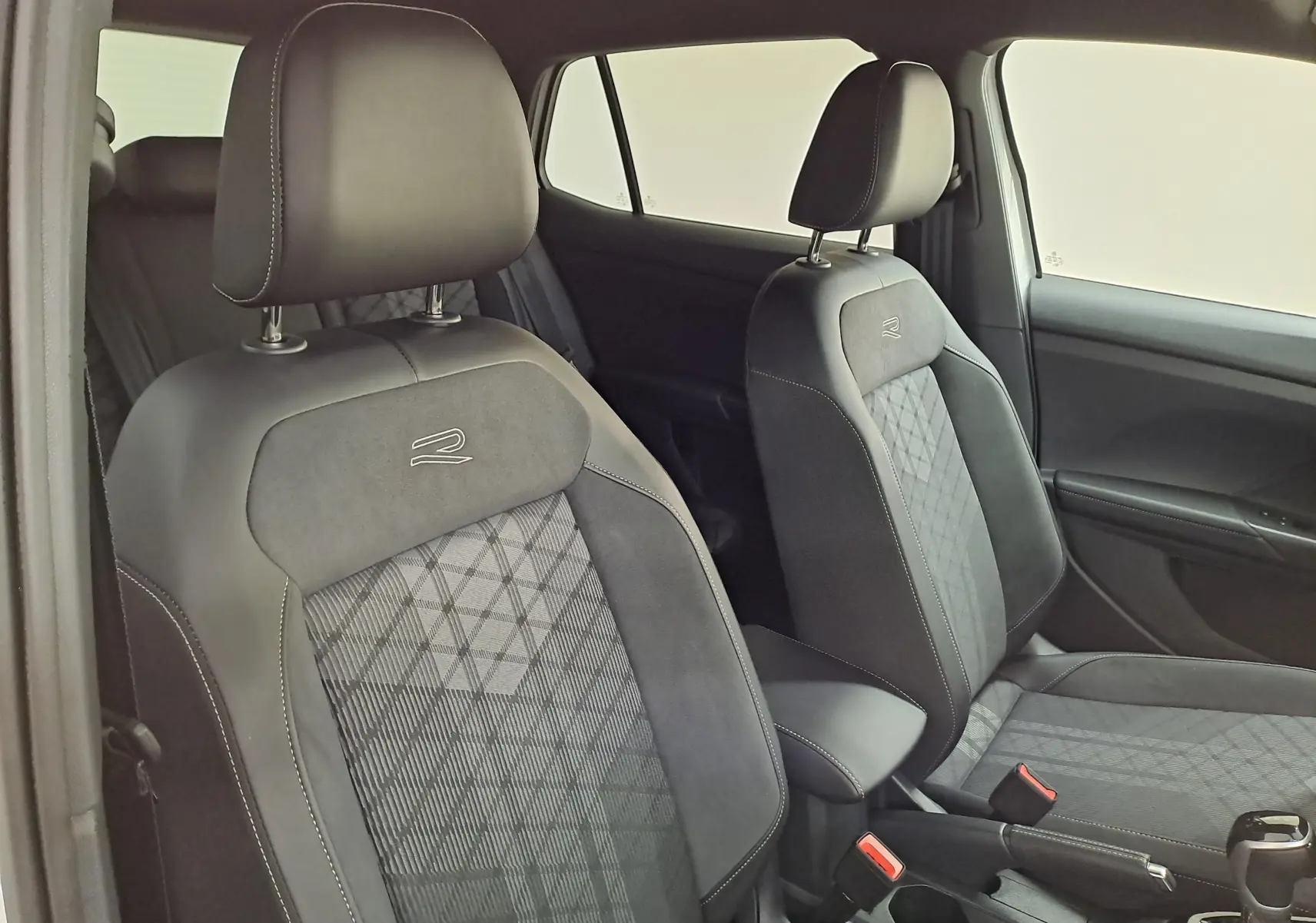 Vue intérieure des sièges avant noirs avec surpiqûres blanches et logo R-Line du Volkswagen T-Cross 2025.