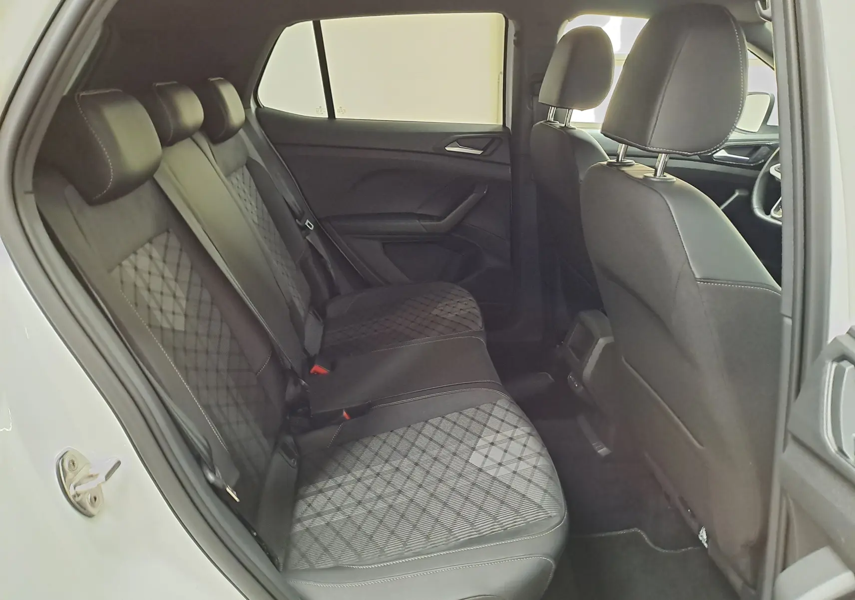 Vue intérieure côté gauche des sièges arrière du Volkswagen T-Cross blanc pur 2025 avec sellerie tissu noir à motif losanges.