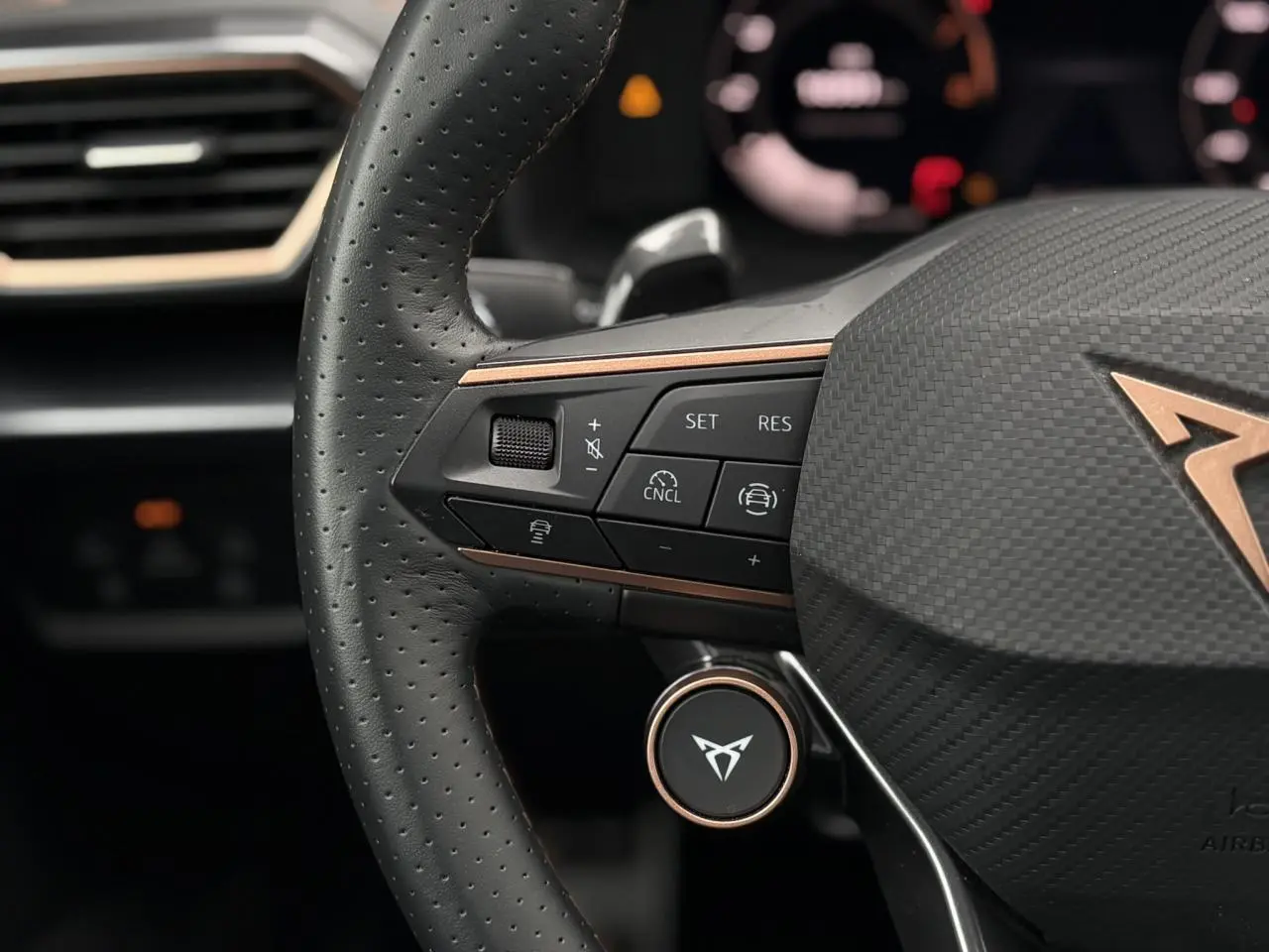Gros plan sur le volant perforé noir avec logo CUPRA cuivré et commandes intégrées, intérieur moderne et élégant.