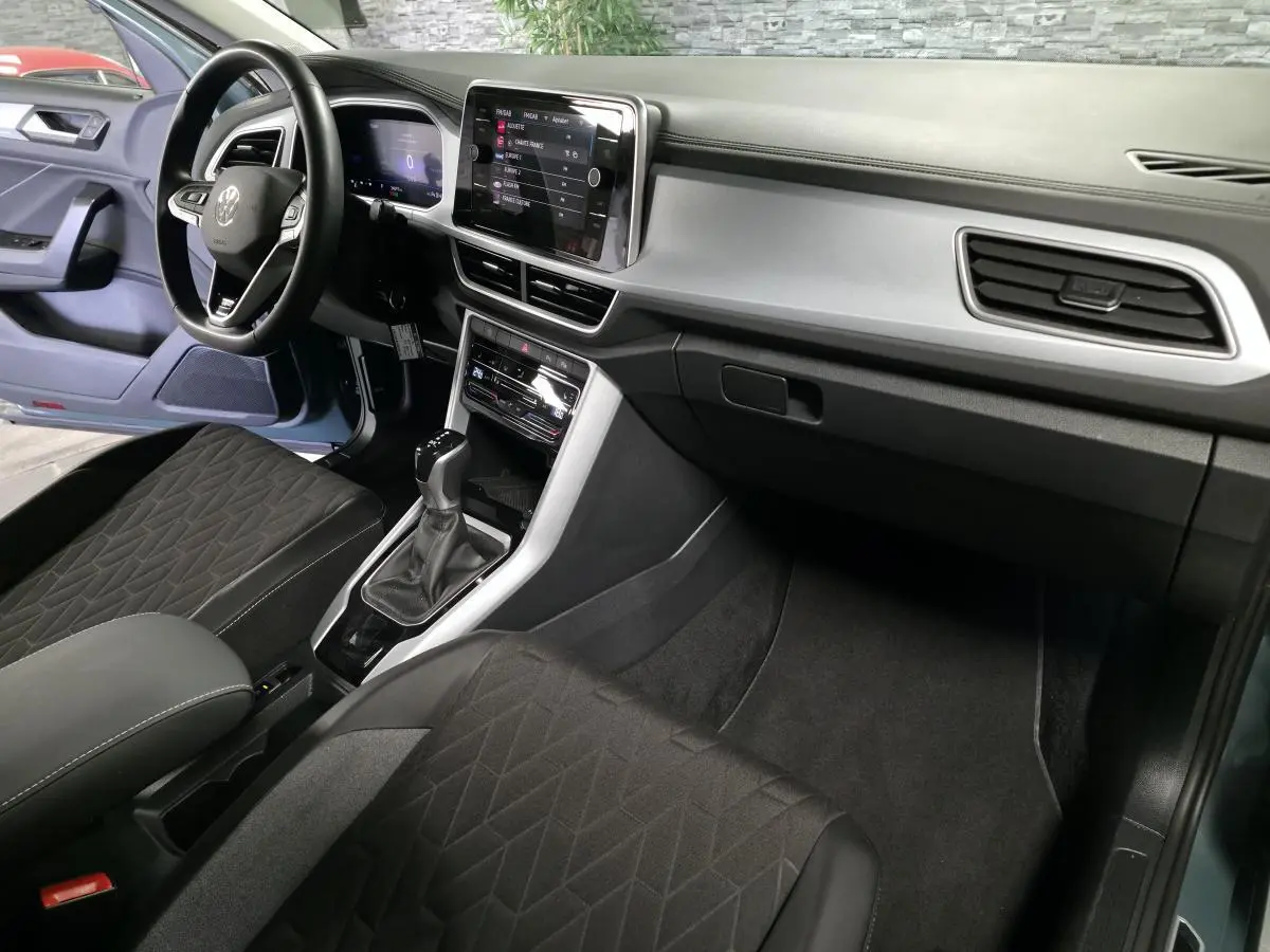 Intérieur avant du Volkswagen T-Roc bleu, vue côté conducteur, tableau de bord digital et sellerie noire.