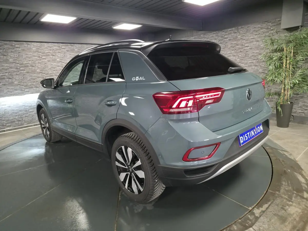 Vue 3/4 arrière droit d'un Volkswagen T-Roc bleu métallisé avec toit noir et badge "GOAL" sur le montant arrière.