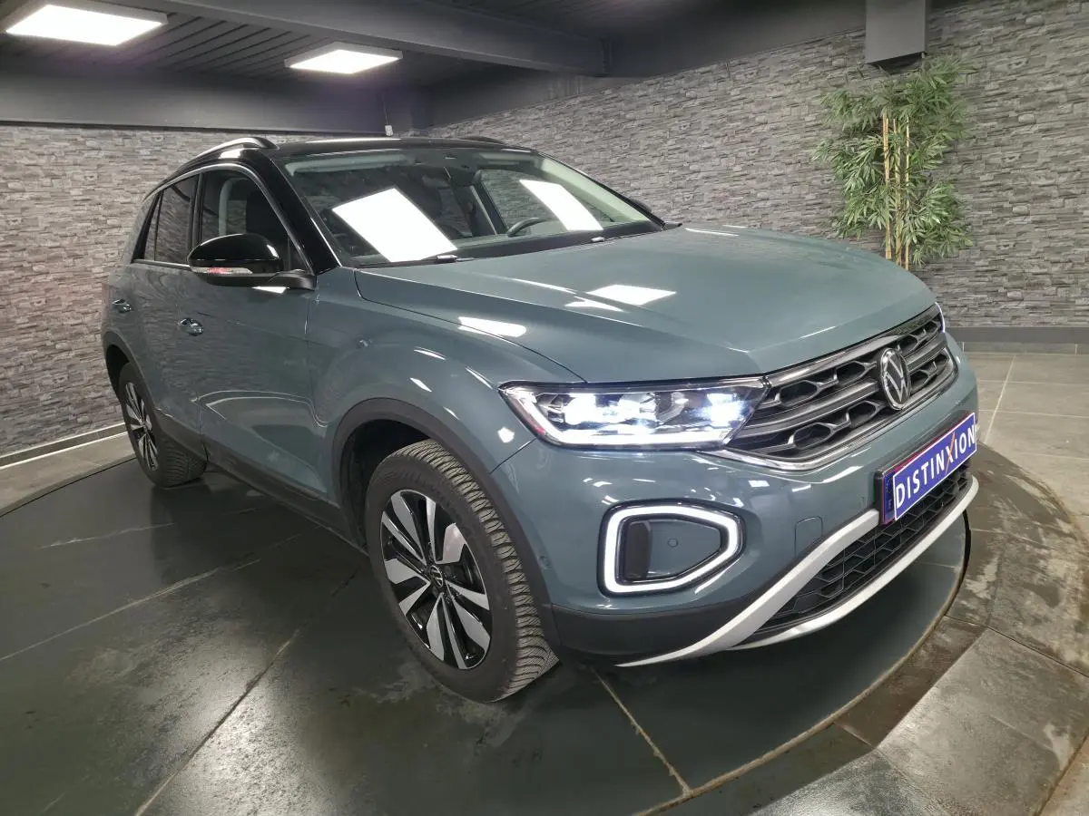 Volkswagen T-Roc bleu 3/4 avant droit avec feux LED allumés et toit noir dans un showroom.