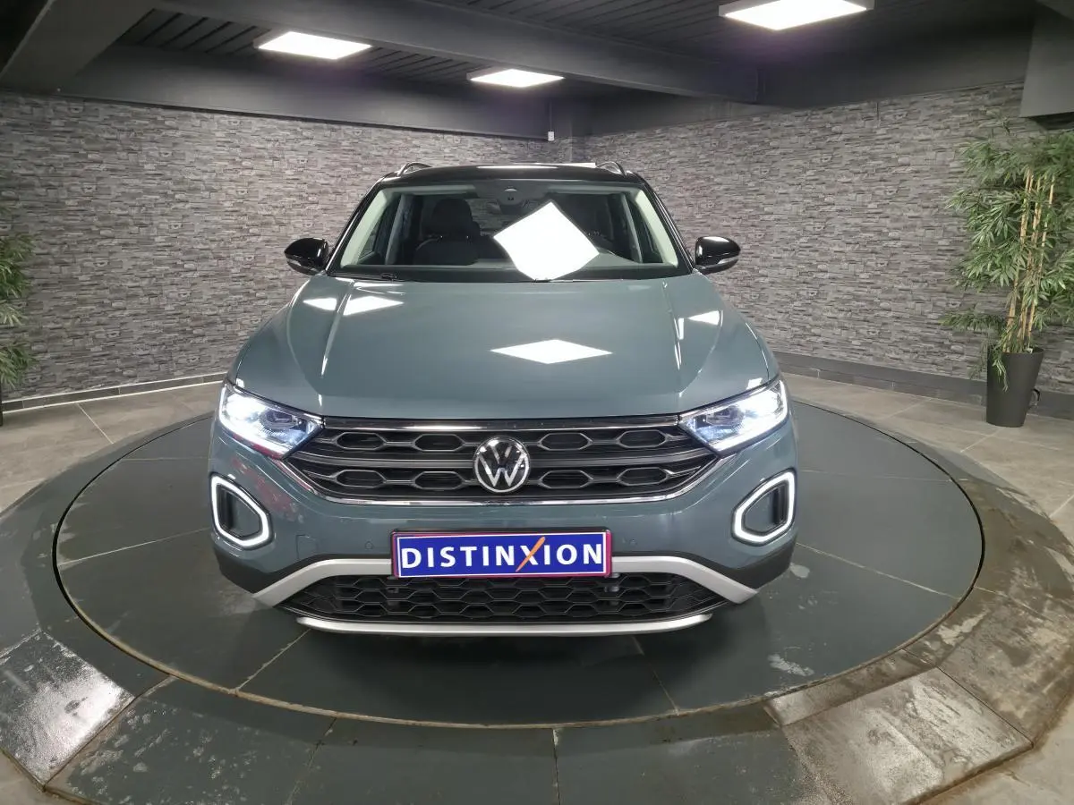 Volkswagen T-Roc bleu en vue frontale, avec calandre noire et feux LED allumés dans un showroom.