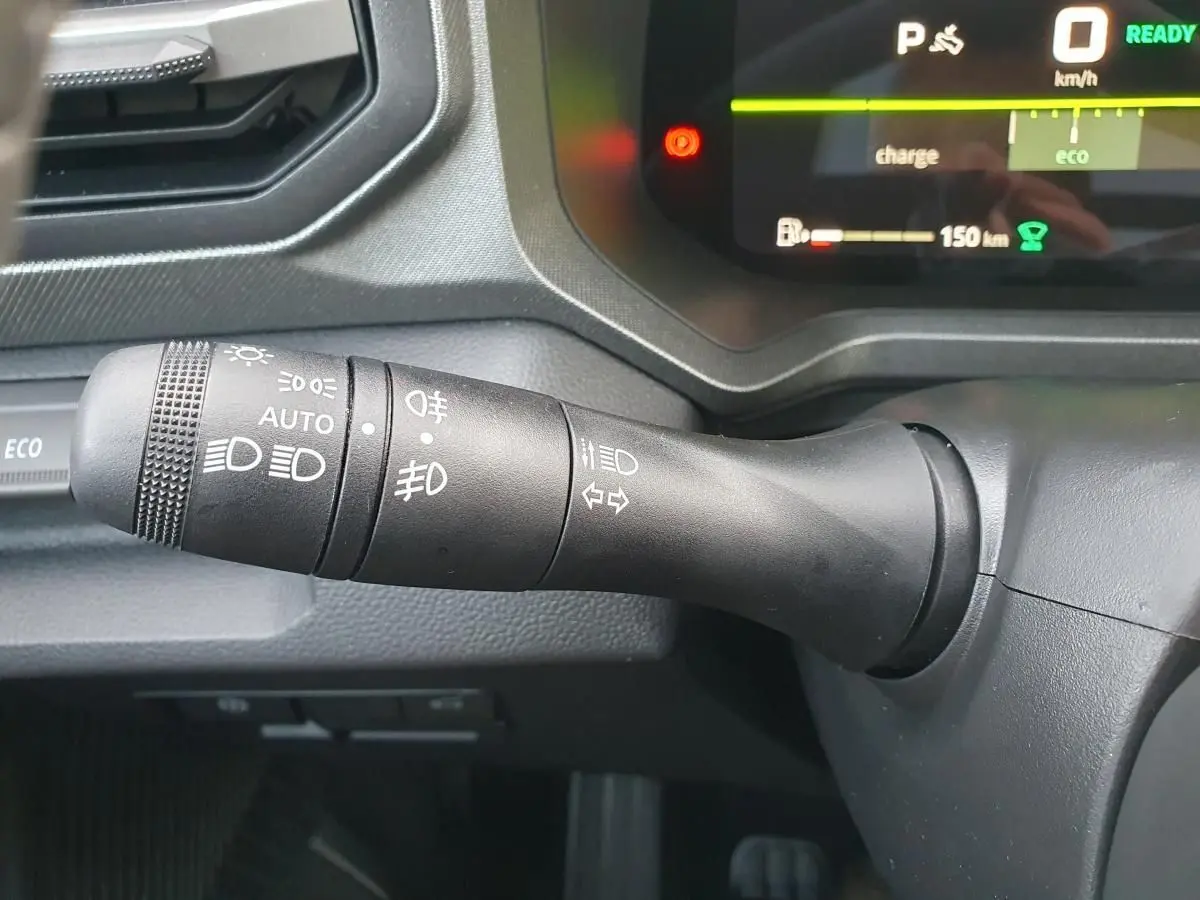 Gros plan sur la commande des feux du DACIA BIGSTER 2026, intérieur noir avec tableau de bord numérique en arrière-plan.