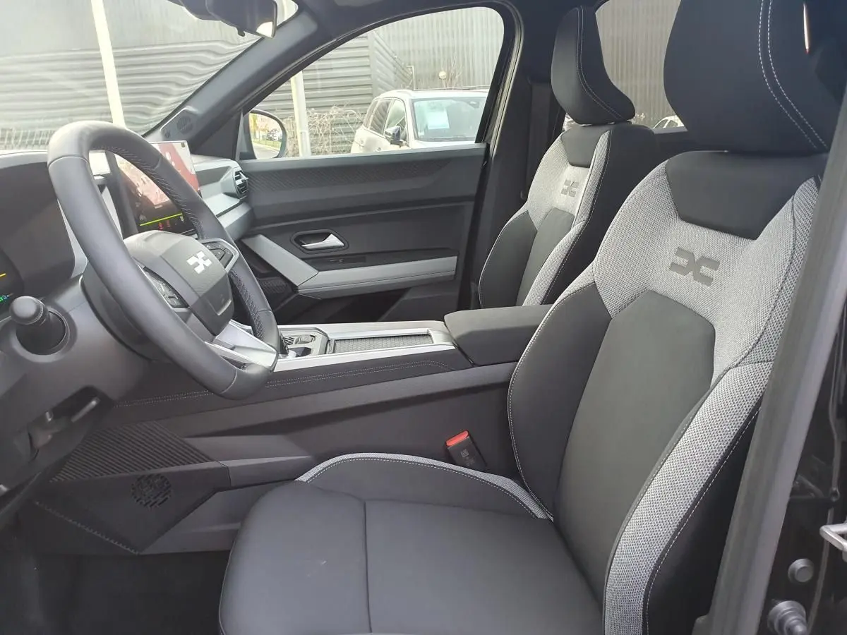 Vue intérieure côté conducteur du Dacia Bigster 2026, sièges bi-matière gris et noir avec logo brodé.