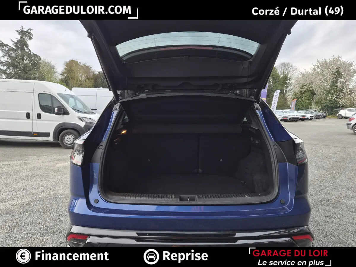 Vue arrière avec coffre ouvert d'une Renault Austral bleu foncé, stationnée en extérieur sur parking.